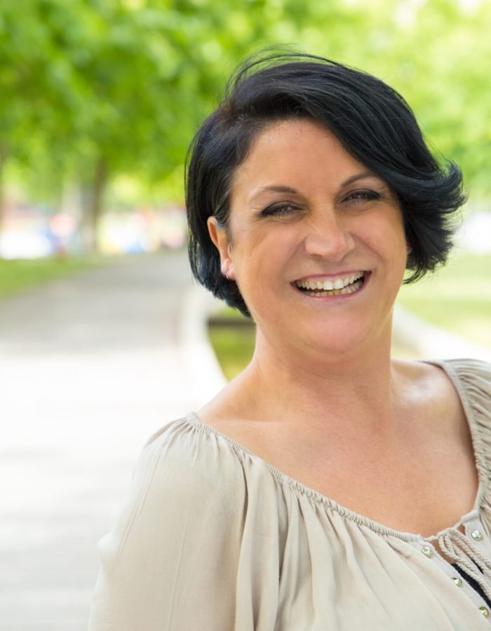 Cheerful excited woman walking in park and laughing. Mature black haired lady enjoying nature outdoors and smiling at camera. Happy woman outdoors concept